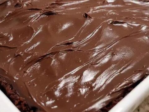 A fork pulling a piece out of a rich, dark chocolate cake with glossy, swirled fudge frosting.