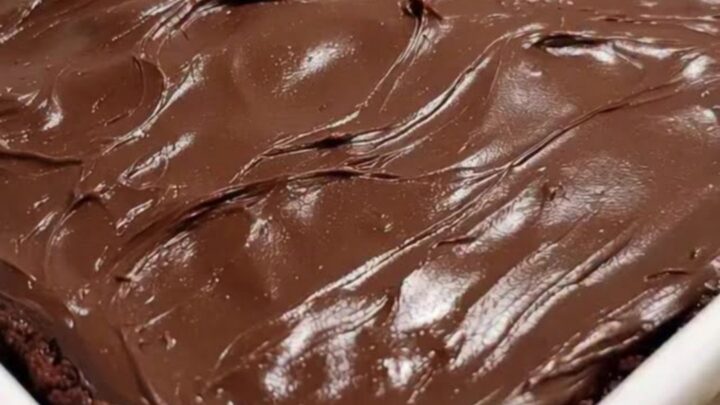 A fork pulling a piece out of a rich, dark chocolate cake with glossy, swirled fudge frosting.