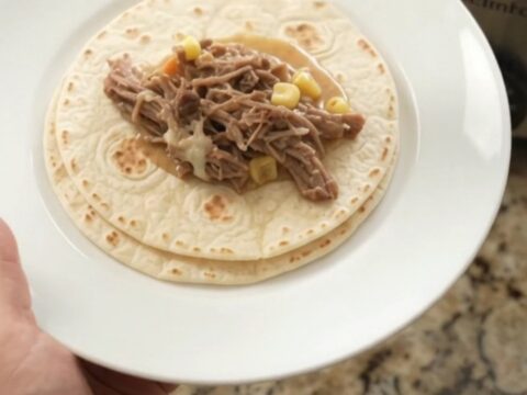 Creamy Crockpot beef barbacoa with hominy and poblanos, topped with melted cheese and served with tortillas