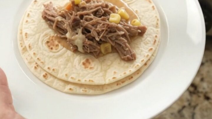 Creamy Crockpot beef barbacoa with hominy and poblanos, topped with melted cheese and served with tortillas