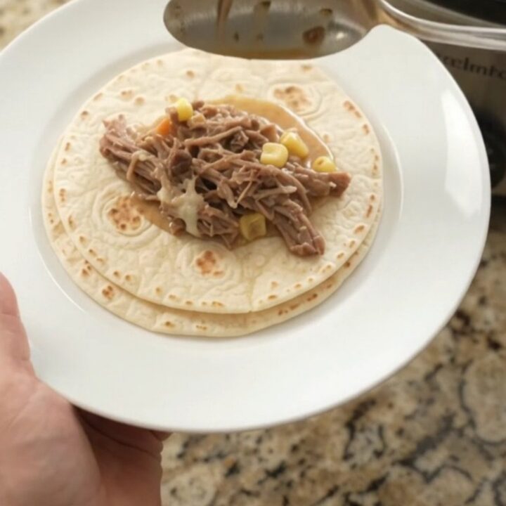 Creamy Crockpot beef barbacoa with hominy and poblanos, topped with melted cheese and served with tortillas