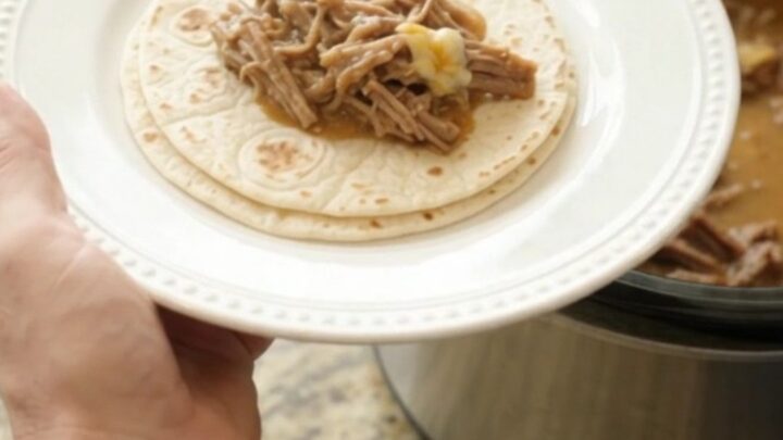 A slow cooker filled with creamy shredded beef barbacoa, pinto beans, and melted cheese sauce