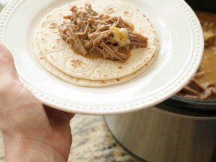 A slow cooker filled with creamy shredded beef barbacoa, pinto beans, and melted cheese sauce