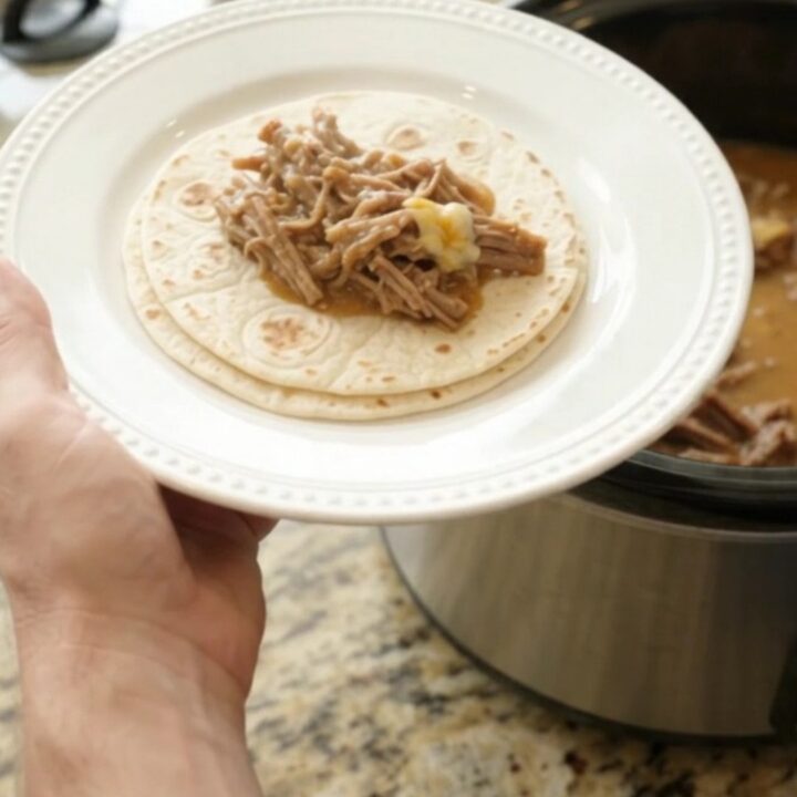 A slow cooker filled with creamy shredded beef barbacoa, pinto beans, and melted cheese sauce