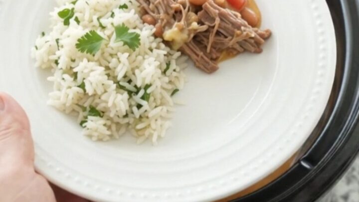 Crockpot full of shredded beef barbacoa in creamy cheddar sauce with pinto beans, topped with cilantro