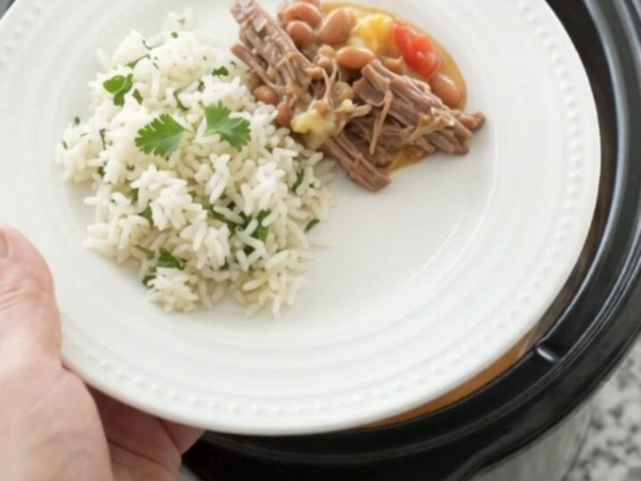 Crockpot full of shredded beef barbacoa in creamy cheddar sauce with pinto beans, topped with cilantro