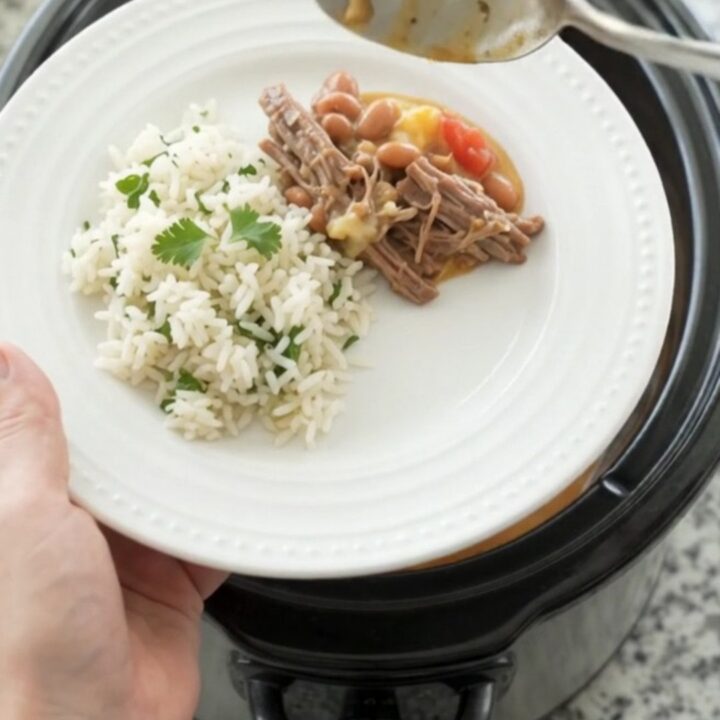 Crockpot full of shredded beef barbacoa in creamy cheddar sauce with pinto beans, topped with cilantro
