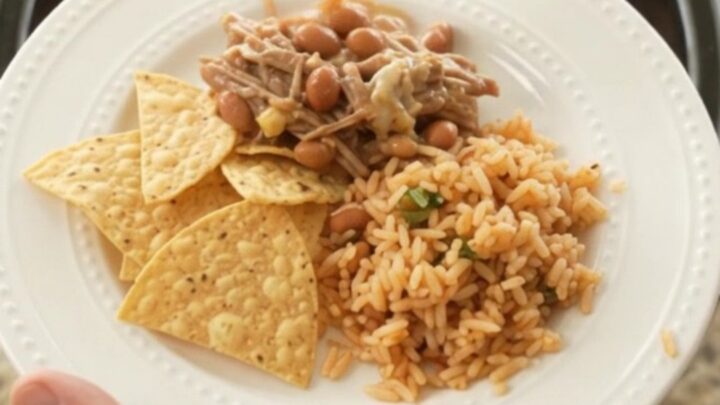 A slow cooker filled with shredded beef barbacoa, pinto beans, and melted pepper jack cheese