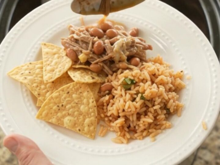 A slow cooker filled with shredded beef barbacoa, pinto beans, and melted pepper jack cheese