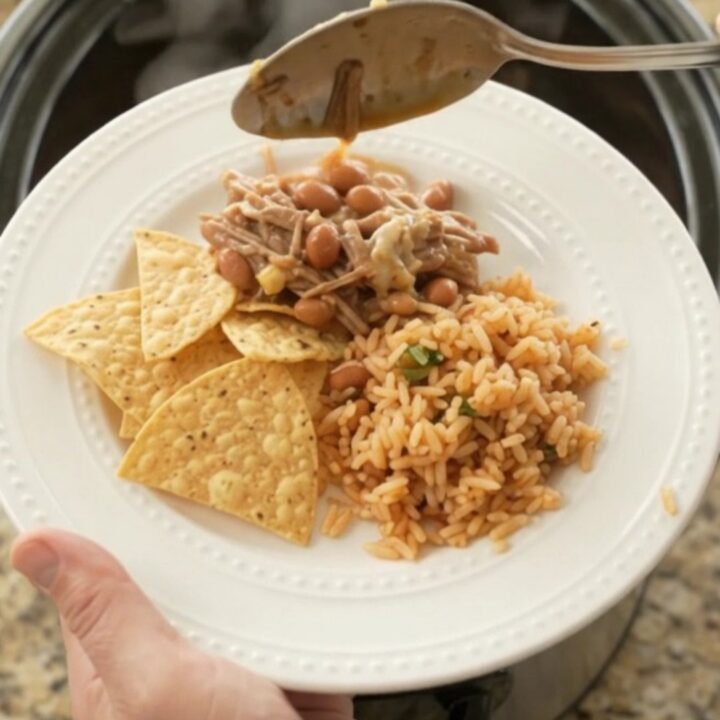 A slow cooker filled with shredded beef barbacoa, pinto beans, and melted pepper jack cheese