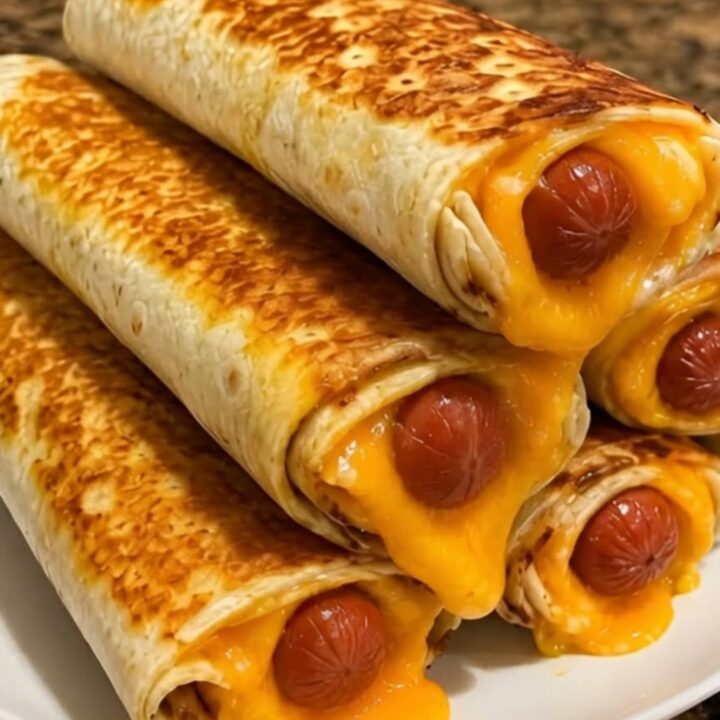 A stack of crispy golden-brown hot dog cheddar wraps on a white plate with melted cheese oozing out.