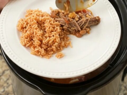 Slow cooker filled with shredded beef barbacoa topped with melted cheese and pinto beans