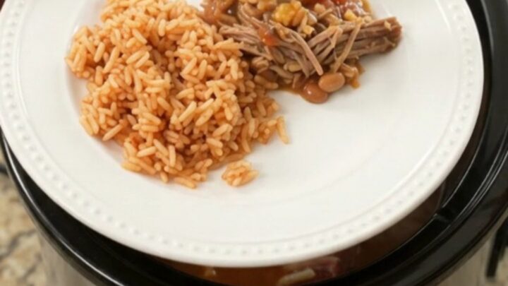 Slow cooker filled with shredded beef barbacoa topped with melted cheese and pinto beans