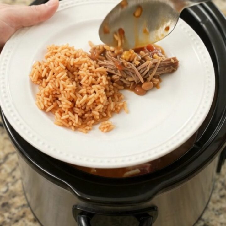 Slow cooker filled with shredded beef barbacoa topped with melted cheese and pinto beans