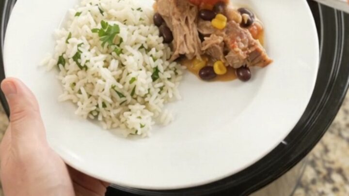 Slow cooker filled with creamy cheddar black bean pork carnitas, topped with melted cheese and fresh cilantro.