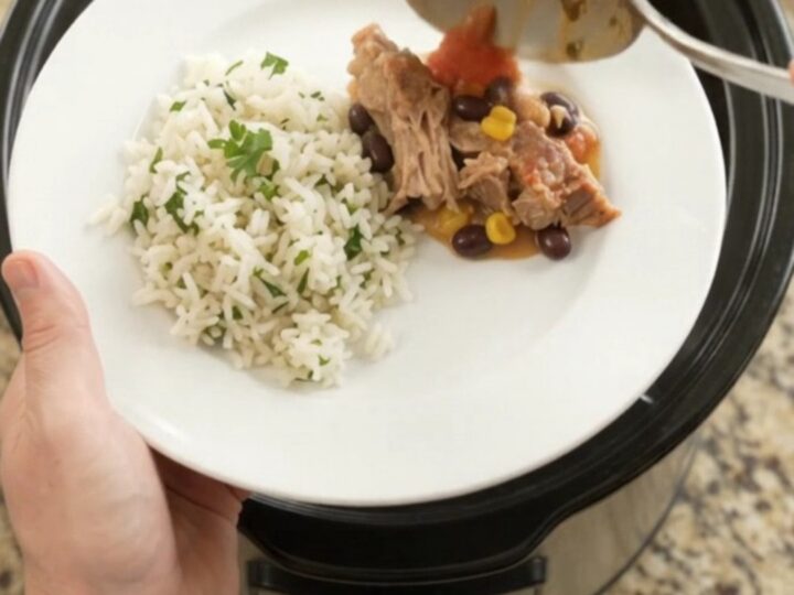Slow cooker filled with creamy cheddar black bean pork carnitas, topped with melted cheese and fresh cilantro.