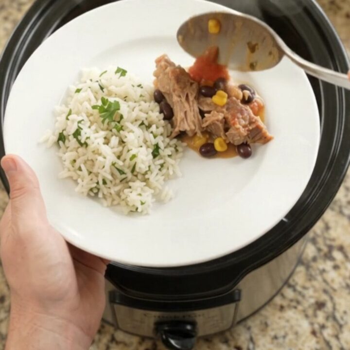 Slow cooker filled with creamy cheddar black bean pork carnitas, topped with melted cheese and fresh cilantro.