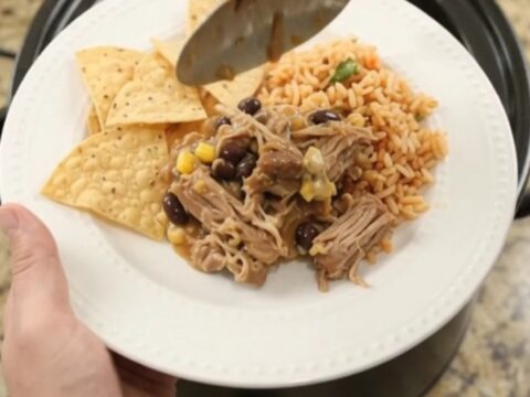Slow cooker pork carnitas with black beans and cheese sauce in a black crockpot