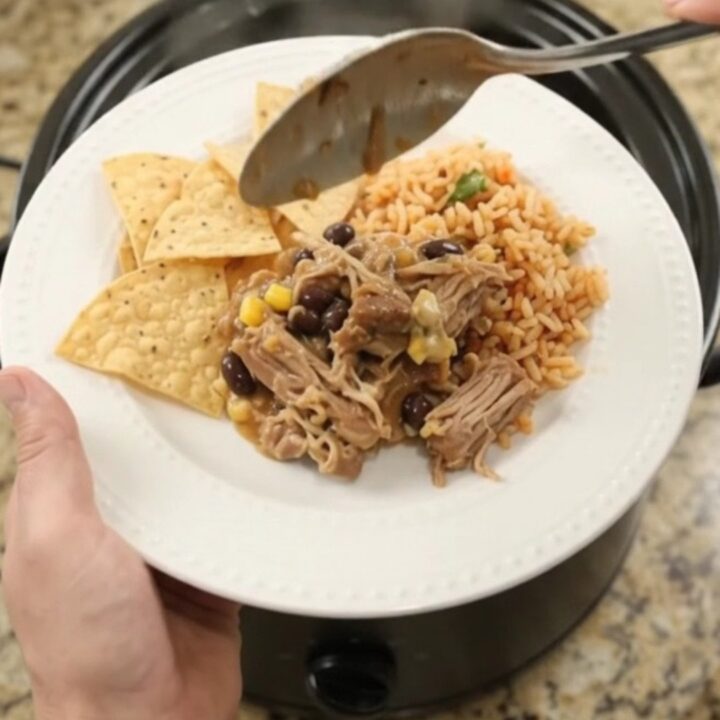 Slow cooker pork carnitas with black beans and cheese sauce in a black crockpot