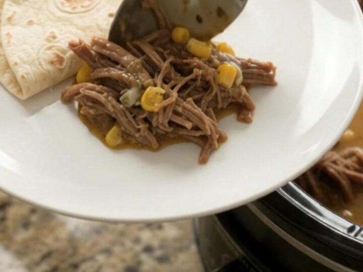 Shredded beef barbacoa in a slow cooker with creamy sauce, corn, and melted cheese