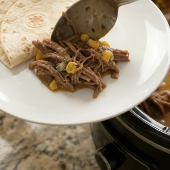 Shredded beef barbacoa in a slow cooker with creamy sauce, corn, and melted cheese
