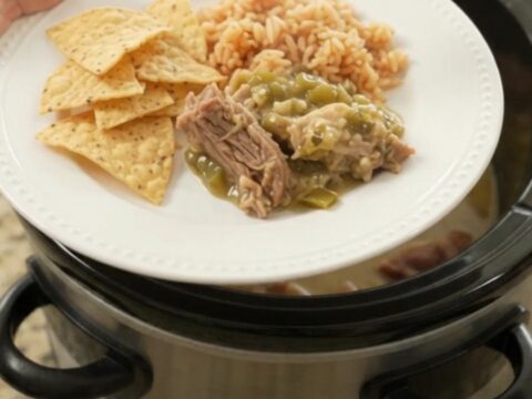 Slow cooker full of creamy salsa verde pork carnitas with melted cheese and steam rising