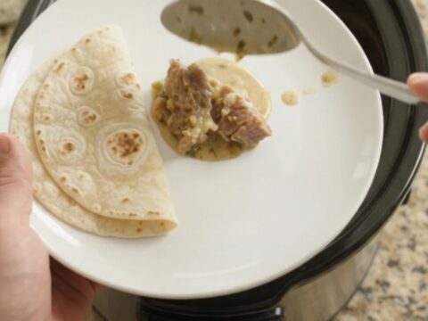 Slow cooker filled with creamy salsa verde pork carnitas, topped with melted Monterey Jack and fresh cilantro