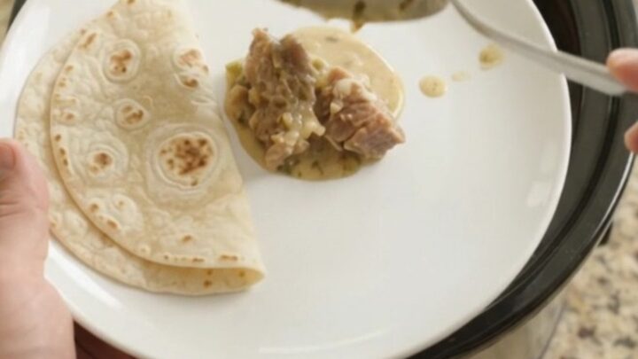Slow cooker filled with creamy salsa verde pork carnitas, topped with melted Monterey Jack and fresh cilantro