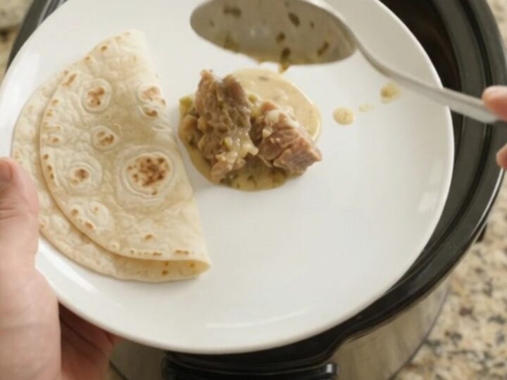 Slow cooker filled with creamy salsa verde pork carnitas, topped with melted Monterey Jack and fresh cilantro