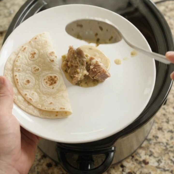 Slow cooker filled with creamy salsa verde pork carnitas, topped with melted Monterey Jack and fresh cilantro