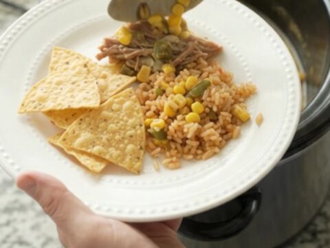 A slow cooker filled with shredded beef barbacoa in a creamy pepper jack queso sauce with corn and green chiles.