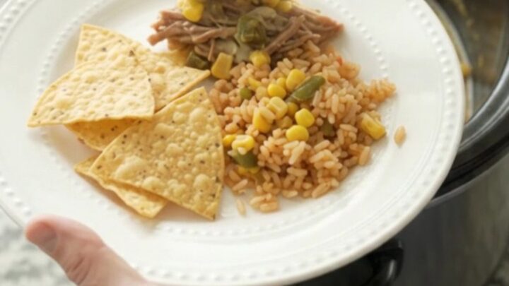 A slow cooker filled with shredded beef barbacoa in a creamy pepper jack queso sauce with corn and green chiles.