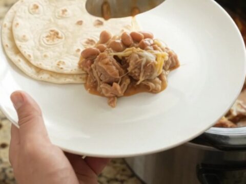 Slow cooker pork carnitas with red sauce and melted cheese in a black crockpot