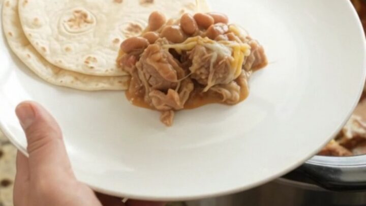 Slow cooker pork carnitas with red sauce and melted cheese in a black crockpot