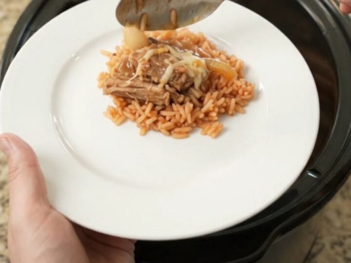 Slow cooker filled with shredded pork, peppers, and melted cheese, with a spoon lifting a portion.