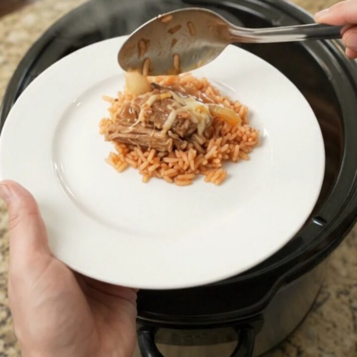 Slow cooker filled with shredded pork, peppers, and melted cheese, with a spoon lifting a portion.
