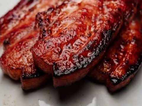 A close-up of thick, perfectly caramelized slices of glazed pork belly on a white plate.