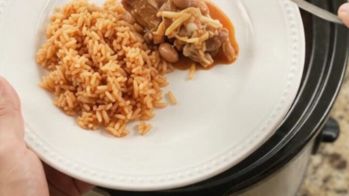 Slow cooker full of pork carnitas with melted Oaxaca cheese and red enchilada sauce, bubbling and steaming