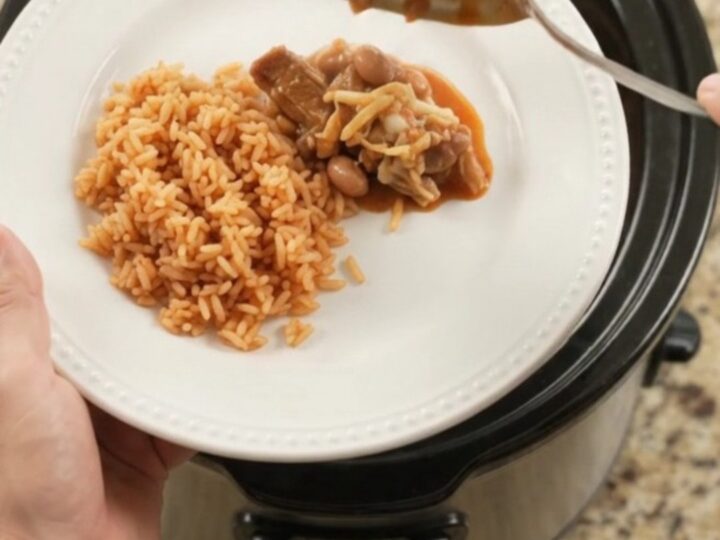 Slow cooker full of pork carnitas with melted Oaxaca cheese and red enchilada sauce, bubbling and steaming
