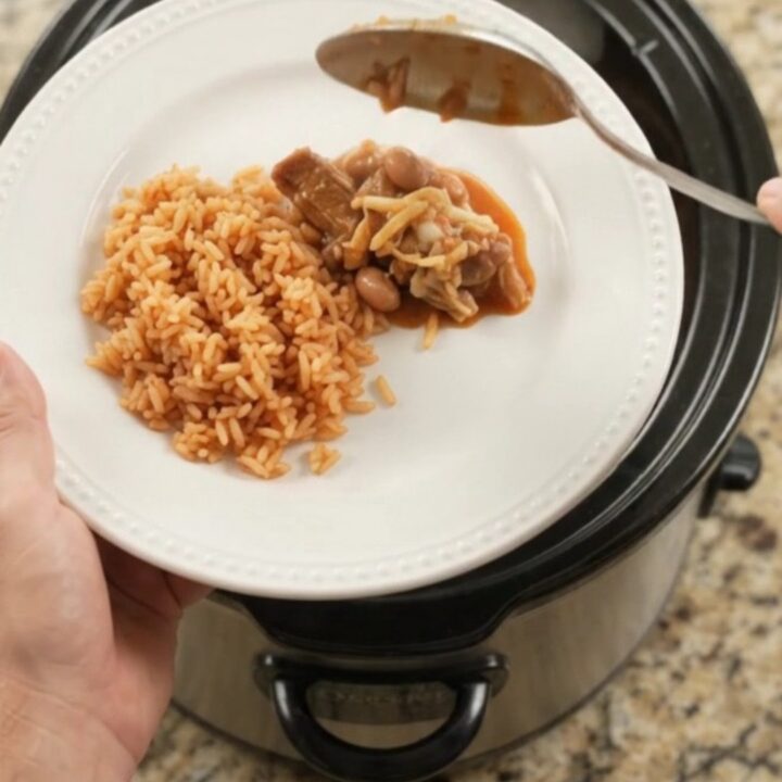 Slow cooker full of pork carnitas with melted Oaxaca cheese and red enchilada sauce, bubbling and steaming