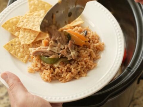 Slow cooker filled with bubbling pork carnitas, peppers, and melted cheese sauce, topped with a spoonful of the mixture.