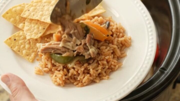 Slow cooker filled with bubbling pork carnitas, peppers, and melted cheese sauce, topped with a spoonful of the mixture.