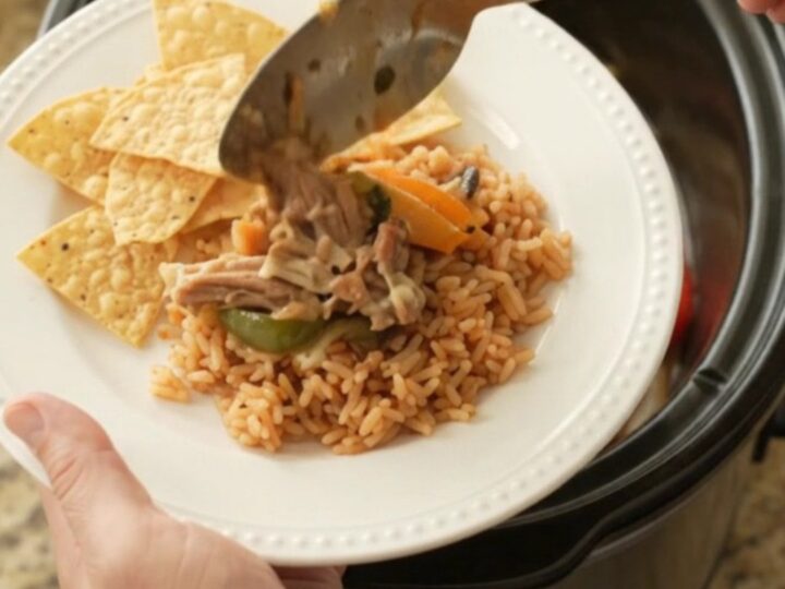 Slow cooker filled with bubbling pork carnitas, peppers, and melted cheese sauce, topped with a spoonful of the mixture.