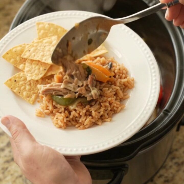 Slow cooker filled with bubbling pork carnitas, peppers, and melted cheese sauce, topped with a spoonful of the mixture.