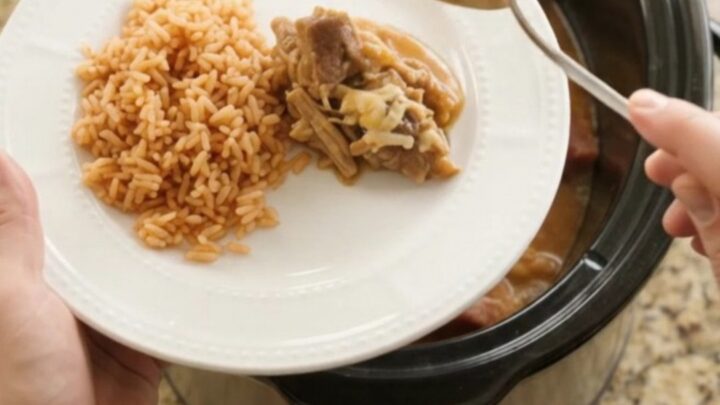 Slow cooker filled with shredded pork carnitas topped with melted cheese and pineapple