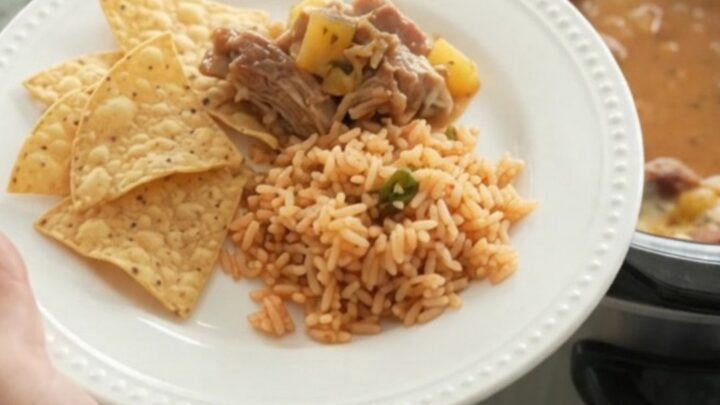 A slow cooker filled with creamy chipotle pineapple pork carnitas, topped with melted cheese and steam rising.