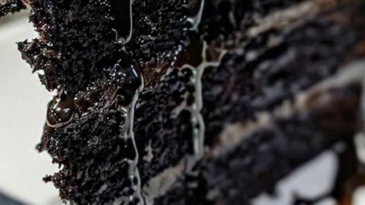 A three-layer black velvet cake with fudge frosting and dripping chocolate ganache on a white plate.