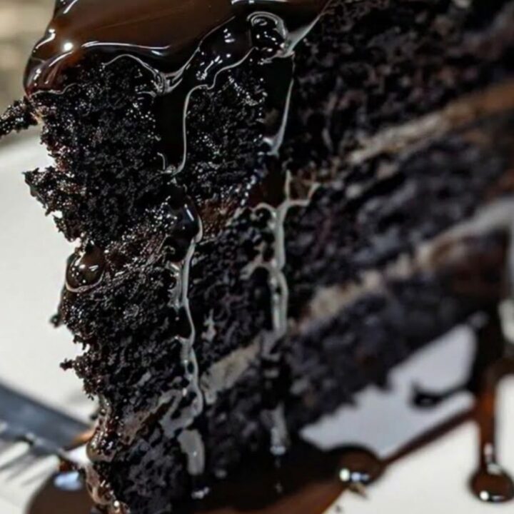 A three-layer black velvet cake with fudge frosting and dripping chocolate ganache on a white plate.
