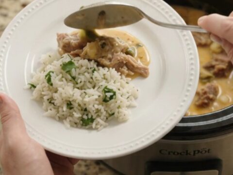 Slow cooker full of creamy cheddar poblano pork carnitas with hominy, steam rising