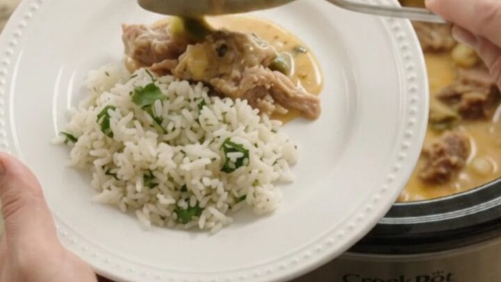 Slow cooker full of creamy cheddar poblano pork carnitas with hominy, steam rising